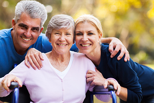 Elderly woman in wheelchair smiling with her husband and daughter smiling on each side of her